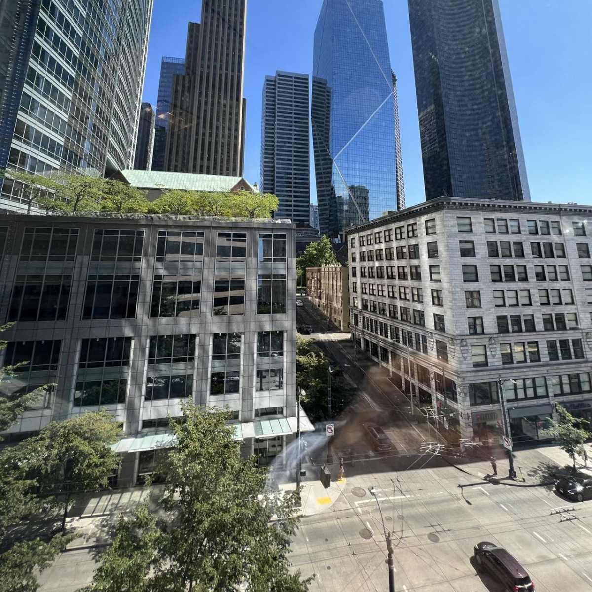 A cityscape with tall glass skyscrapers and a mix of modern and historical buildings under a clear blue sky.