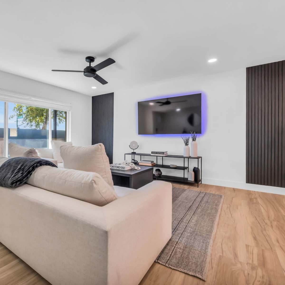 A modern living room features a light-colored sofa, a coffee table, and a wall-mounted television against a backdrop of wood paneling.
