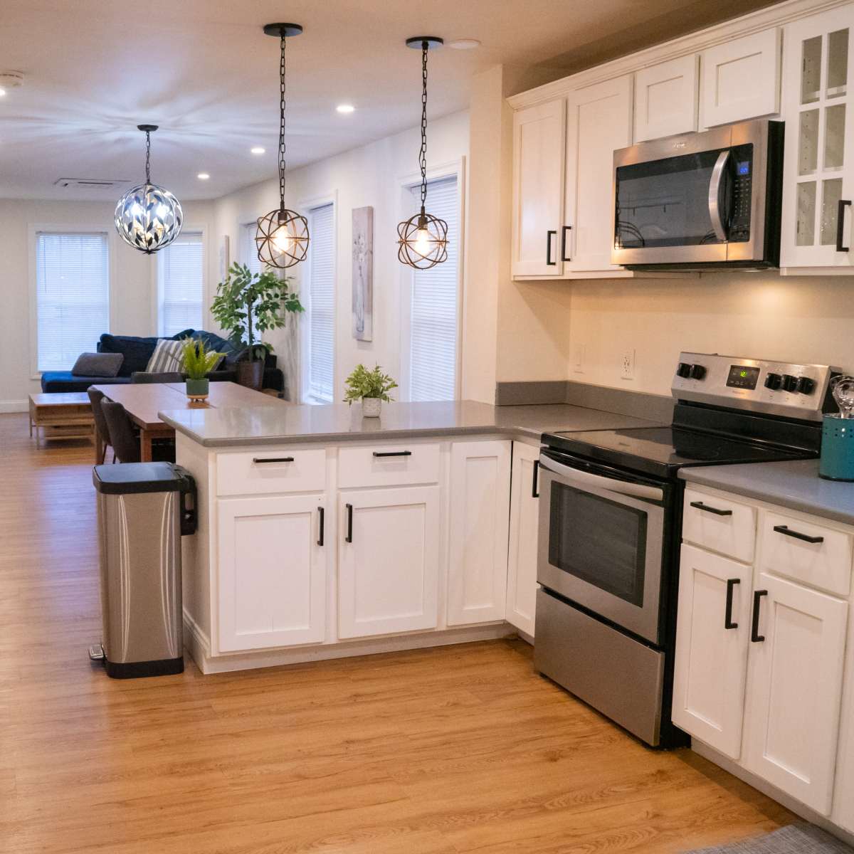 A modern kitchen with white cabinetry, stainless steel appliances, and a countertop that opens to a living area with a sofa and a dining table.