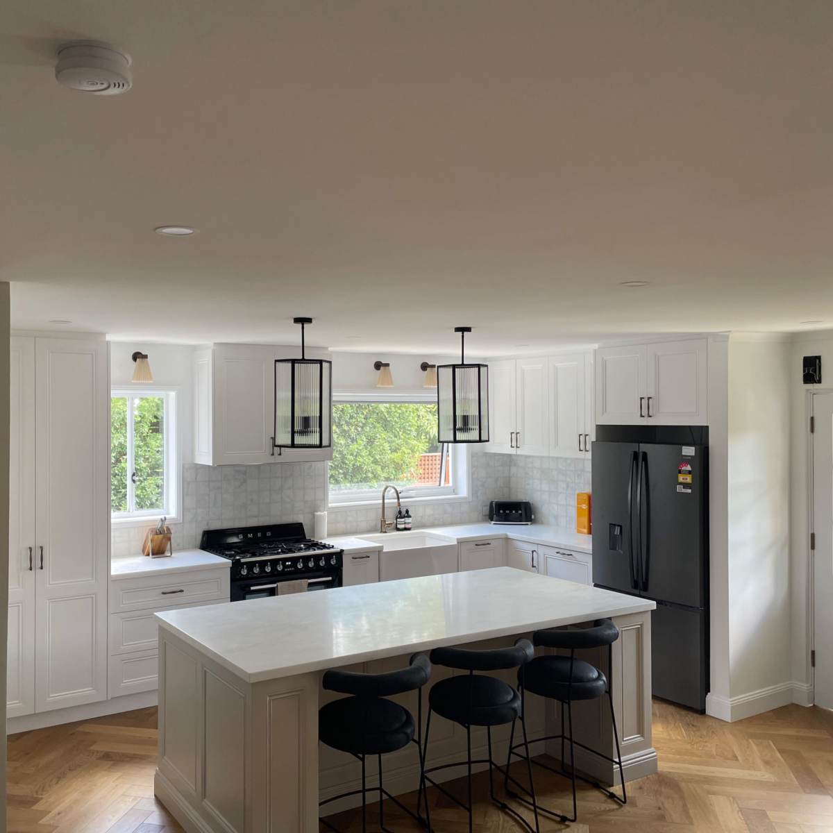 A modern kitchen featuring white cabinetry, a central island with bar stools, and large windows that provide natural light.