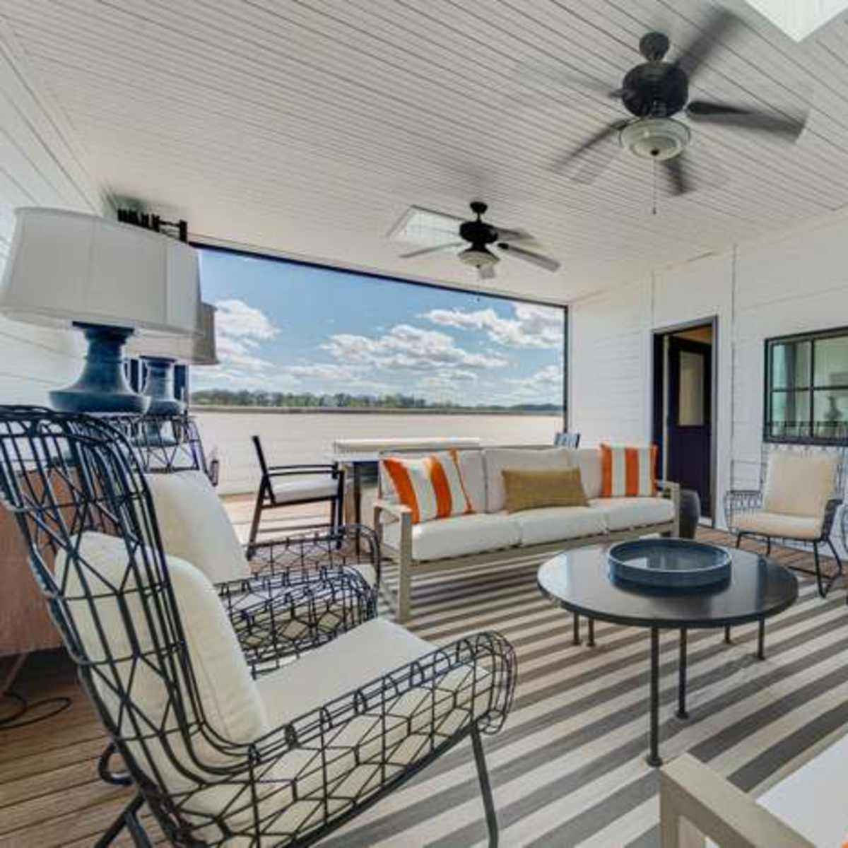 A covered outdoor seating area with metal framed chairs and sofa, a round table, and a light fixture, all arranged on a striped rug.