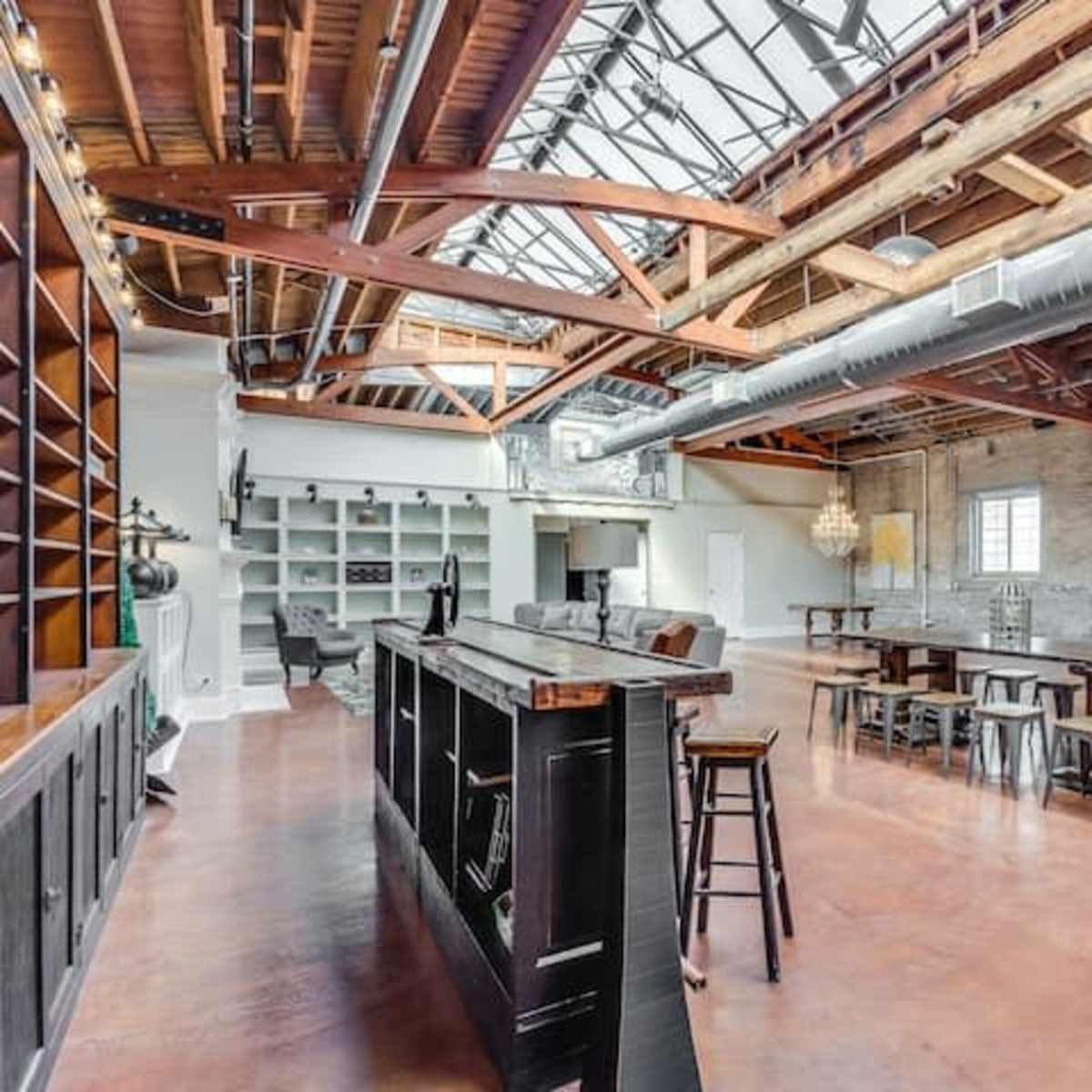 A spacious loft with exposed wooden beams, large windows, and a mix of modern and rustic furniture.