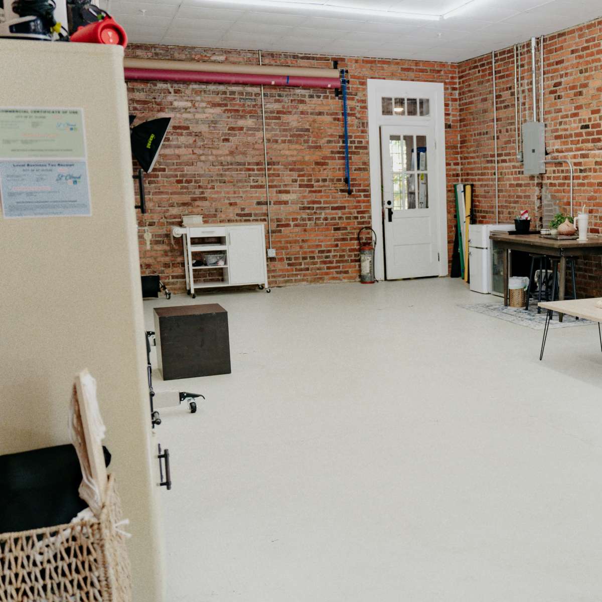 A spacious room with exposed brick walls, a green armchair, a black couch, a small coffee table, and a doorway leading to another area.