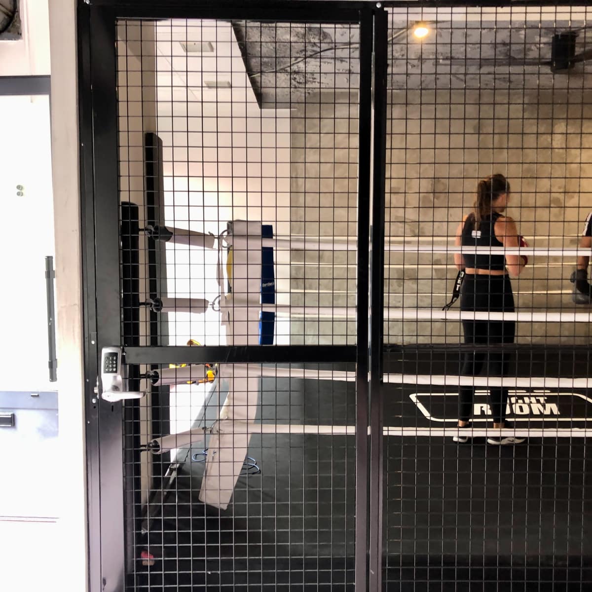 A fenced entrance to a gym area, with a mirrored wall and workout equipment visible inside.
