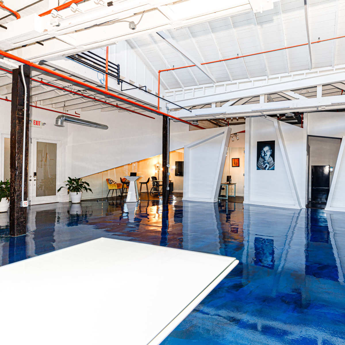 A spacious, modern interior with polished blue floors, white walls, and unique angular partitions, featuring a mix of furniture and greenery.