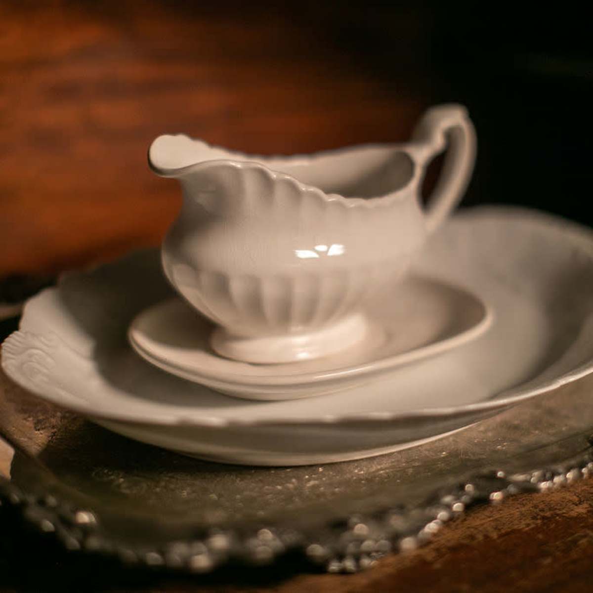 A white ceramic creamer sits atop a small plate, which is placed on a larger plate, all arranged on a silver tray.
