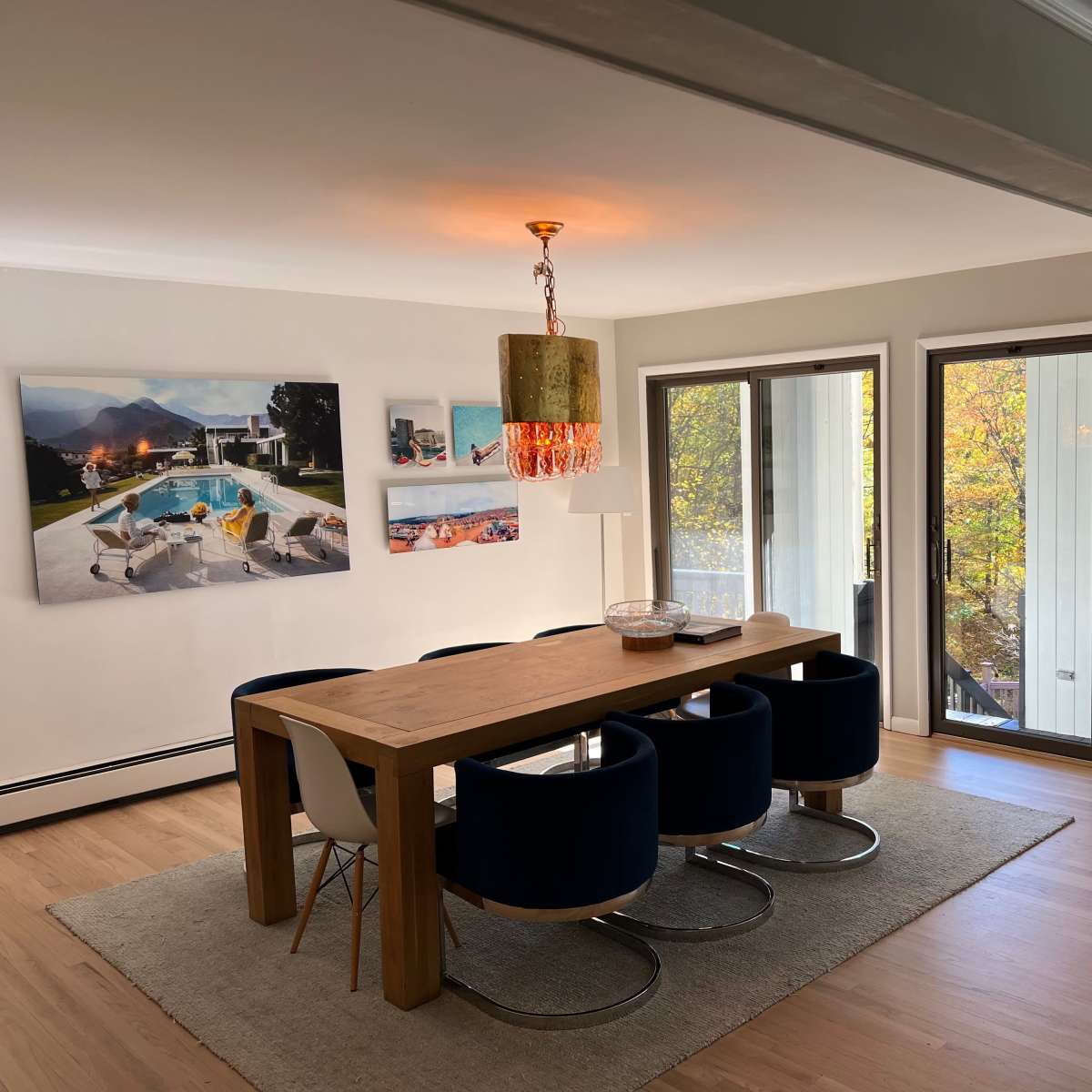 A spacious dining area features a wooden table surrounded by blue chairs, with large windows offering views of autumn foliage.