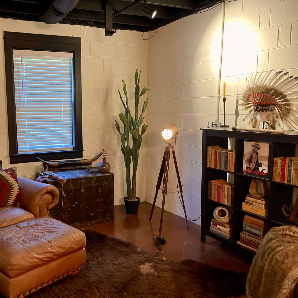 A cozy room featuring a leather chaise lounge, a large plant, a bookshelf filled with books, and a vintage-style lamp.