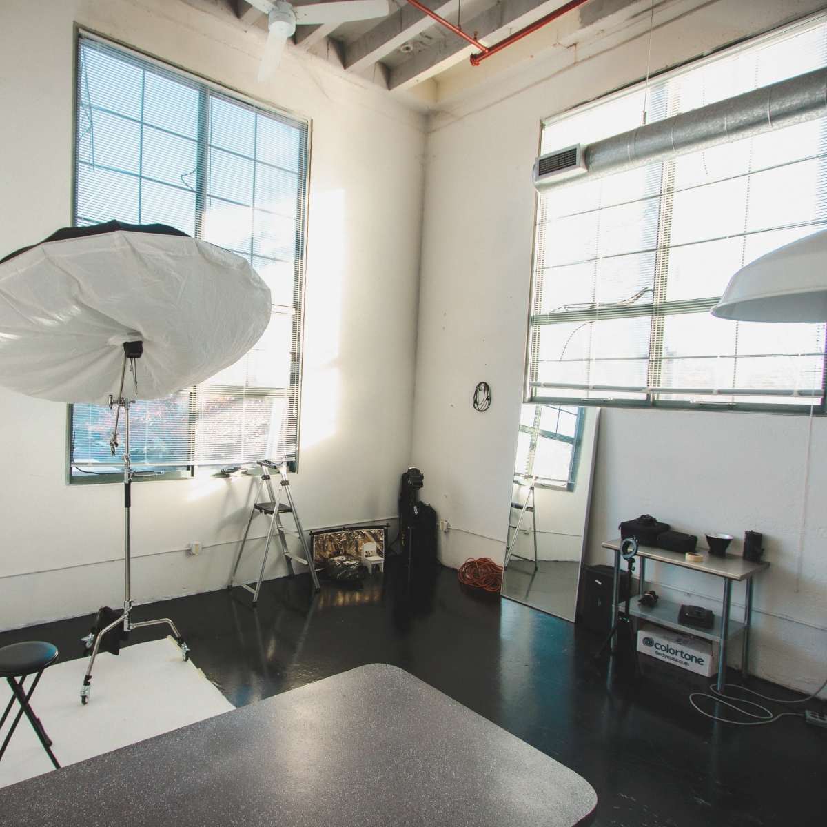 A well-lit photography studio with large windows, a light umbrella, a stool, and colorful backdrops.