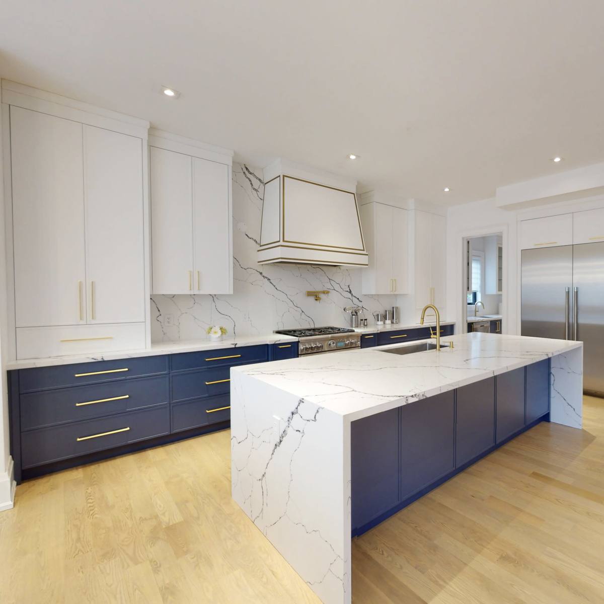 The kitchen features an island with a marble countertop, navy blue cabinetry, and stainless steel appliances, creating an open and modern layout.
