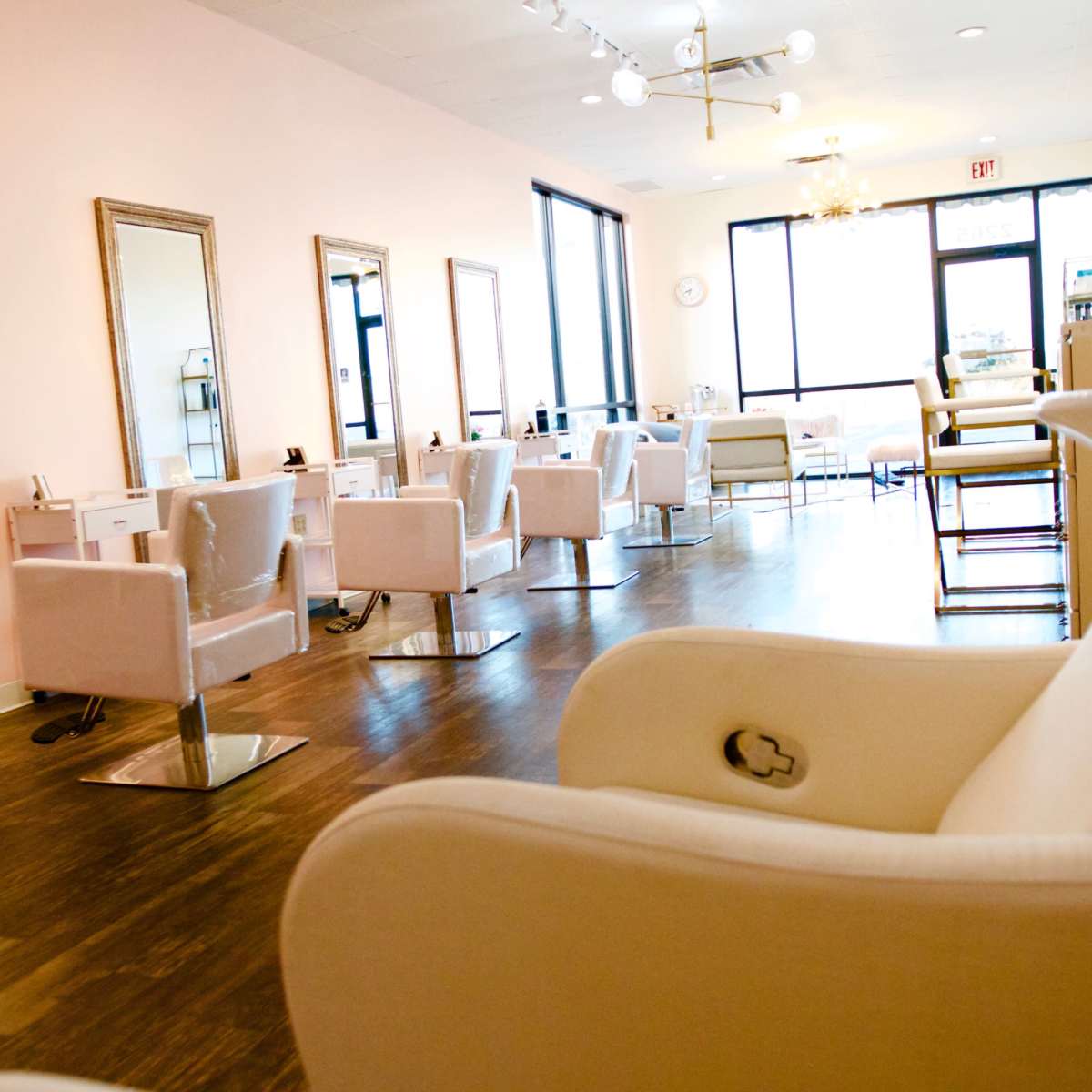 A modern hair salon with white chairs, large mirrors, and a bright, open space with natural light.