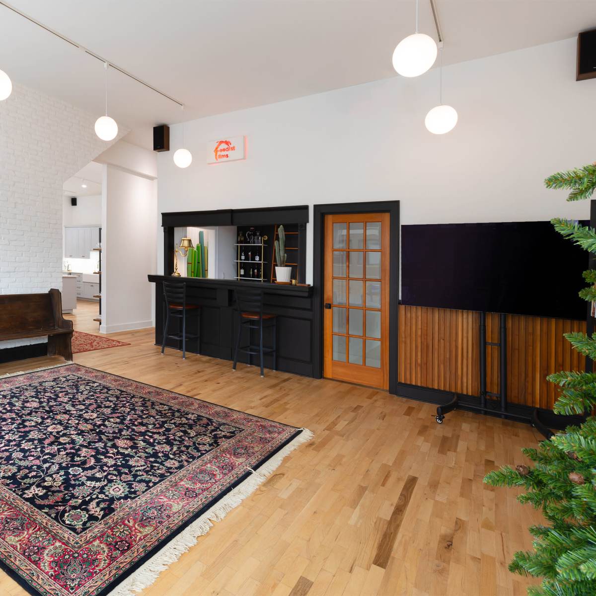 A spacious room with a wooden bench, a patterned area rug, a bar counter, and a few modern light fixtures hanging from the ceiling.