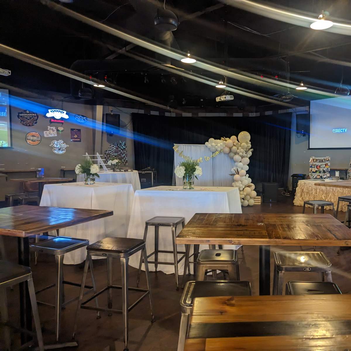 An indoor event space with decorated tables, a backdrop of balloons, and various seating arrangements.