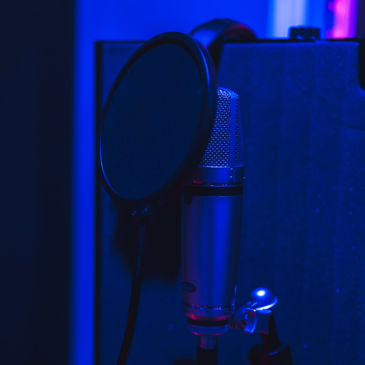 A microphone with a pop filter is mounted on a stand in a dimly lit recording studio.