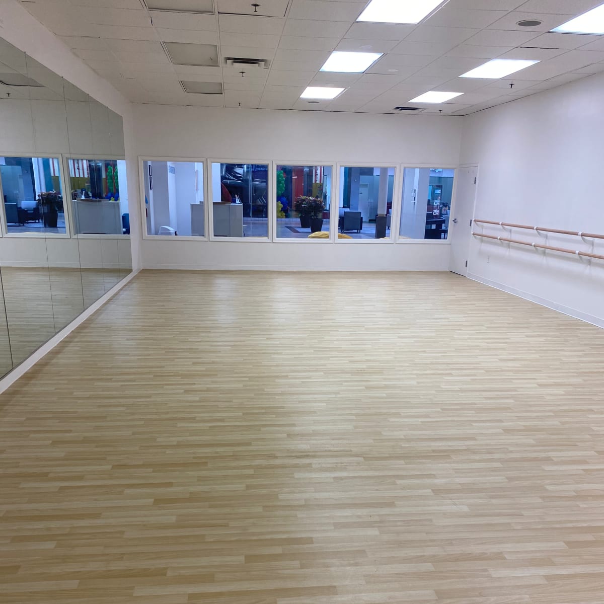 A spacious dance studio with wooden flooring, large mirrors on one wall, and bright natural light coming through the windows.