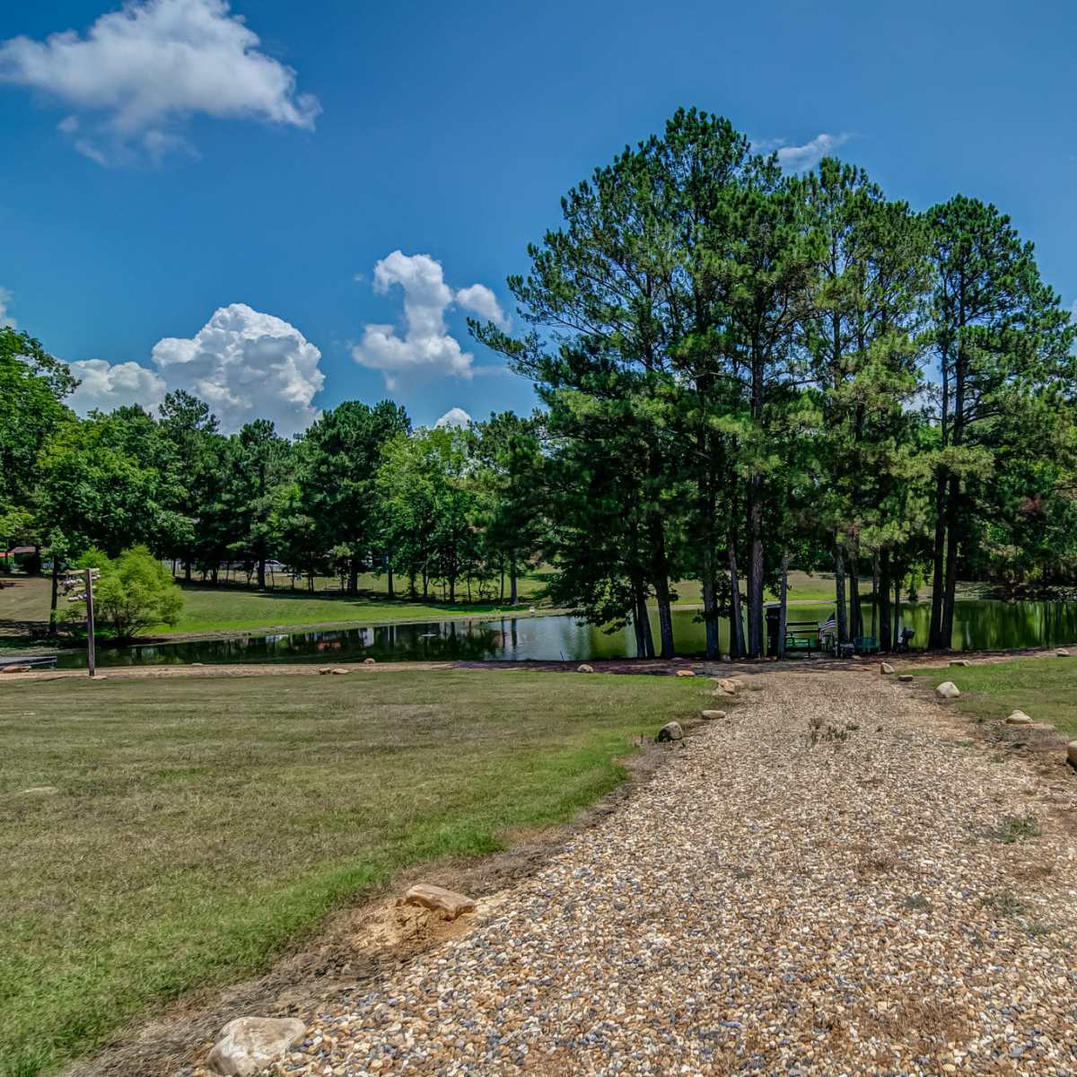 A gravel path leads to a small pond surrounded by trees in a green landscape.