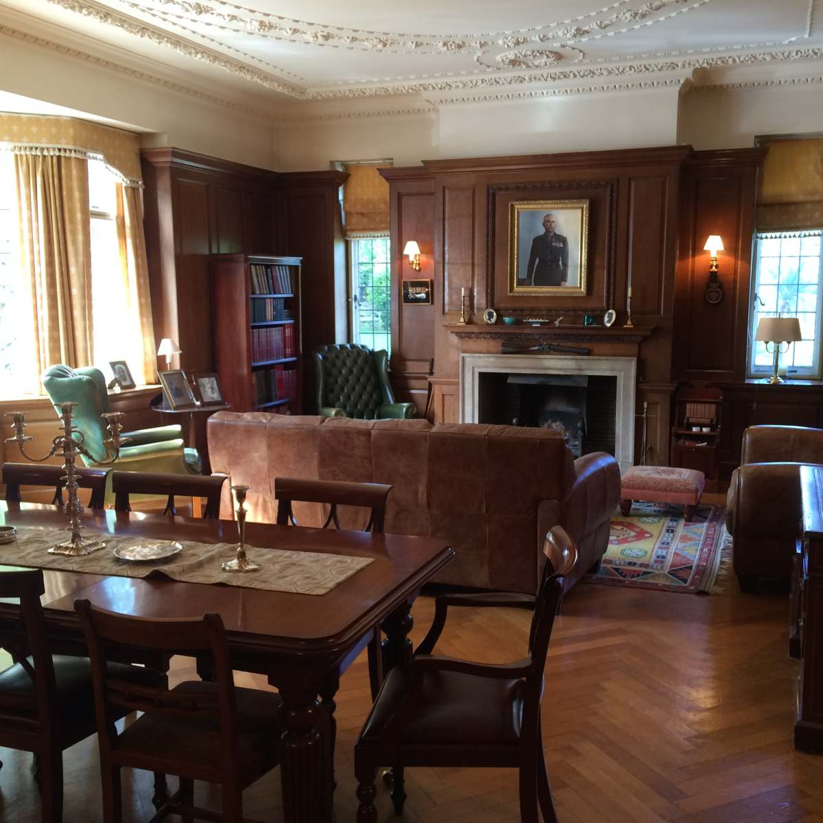 A well-furnished living room with wooden paneling, a fireplace, and various seating arrangements including a green armchair and a brown sofa.