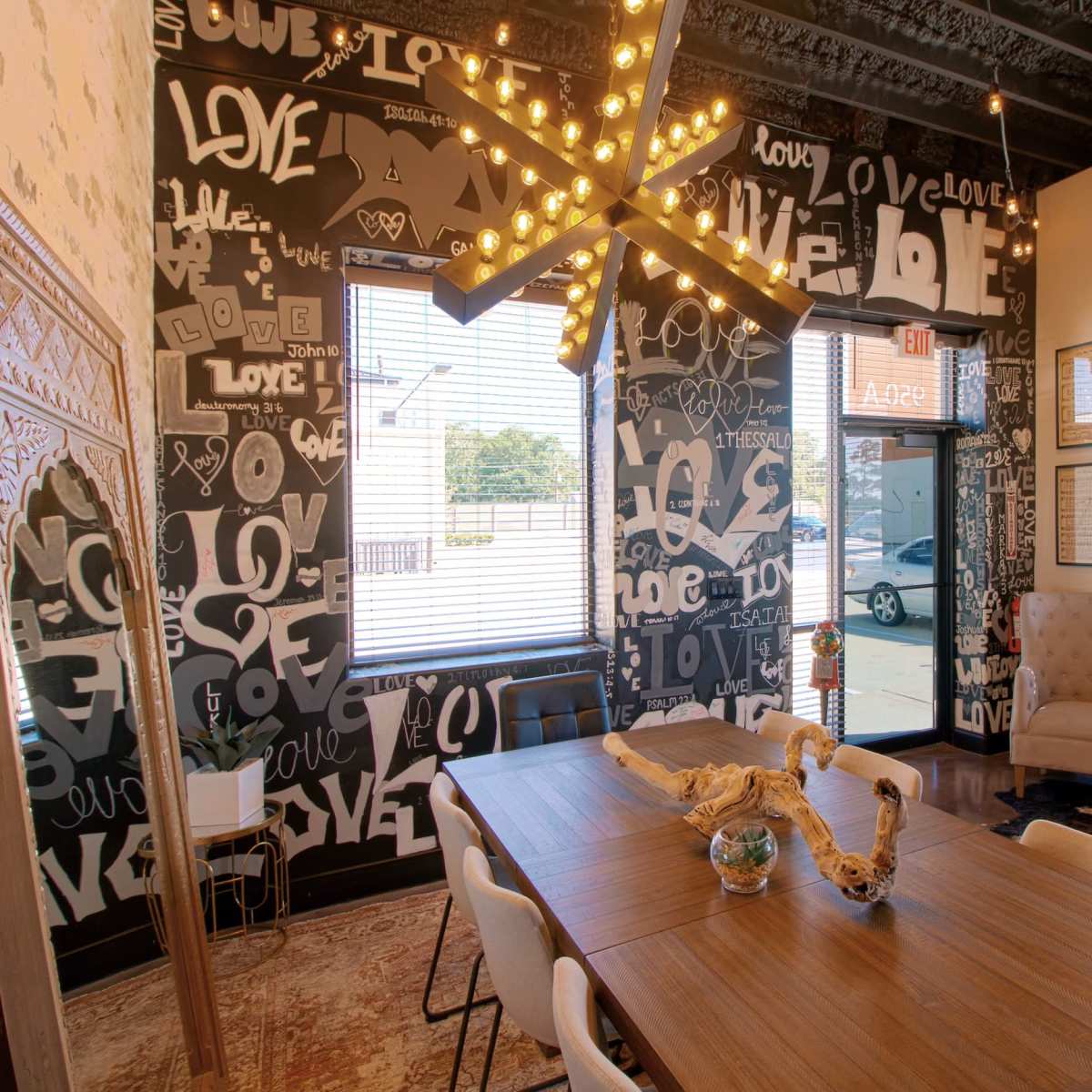 The scene shows a modern dining area with a large wooden table surrounded by white chairs, set against a wall adorned with black and white typographic art that features the word "love."
