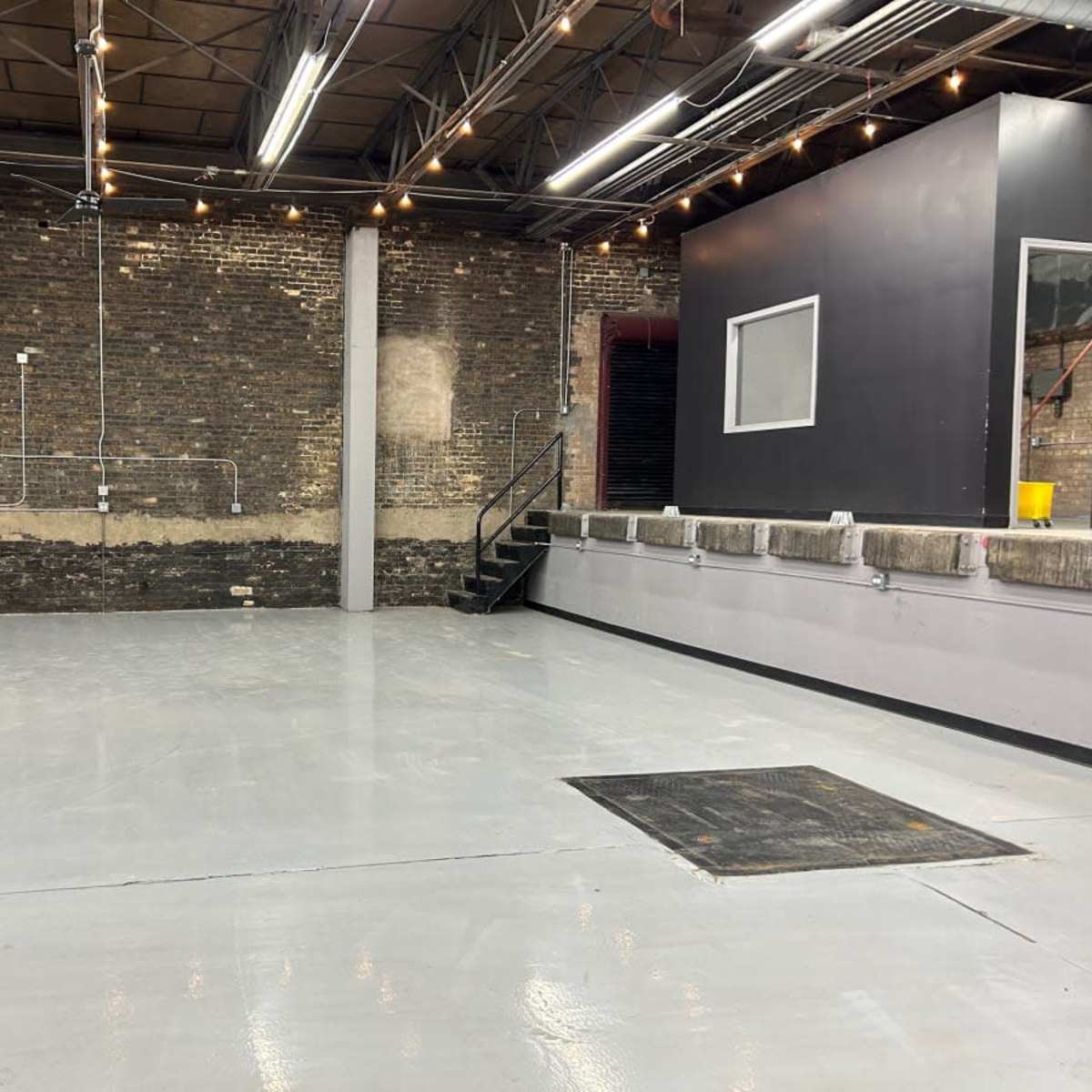 A spacious, industrial-style room with exposed brick walls, polished concrete flooring, and a staircase leading to a raised area.