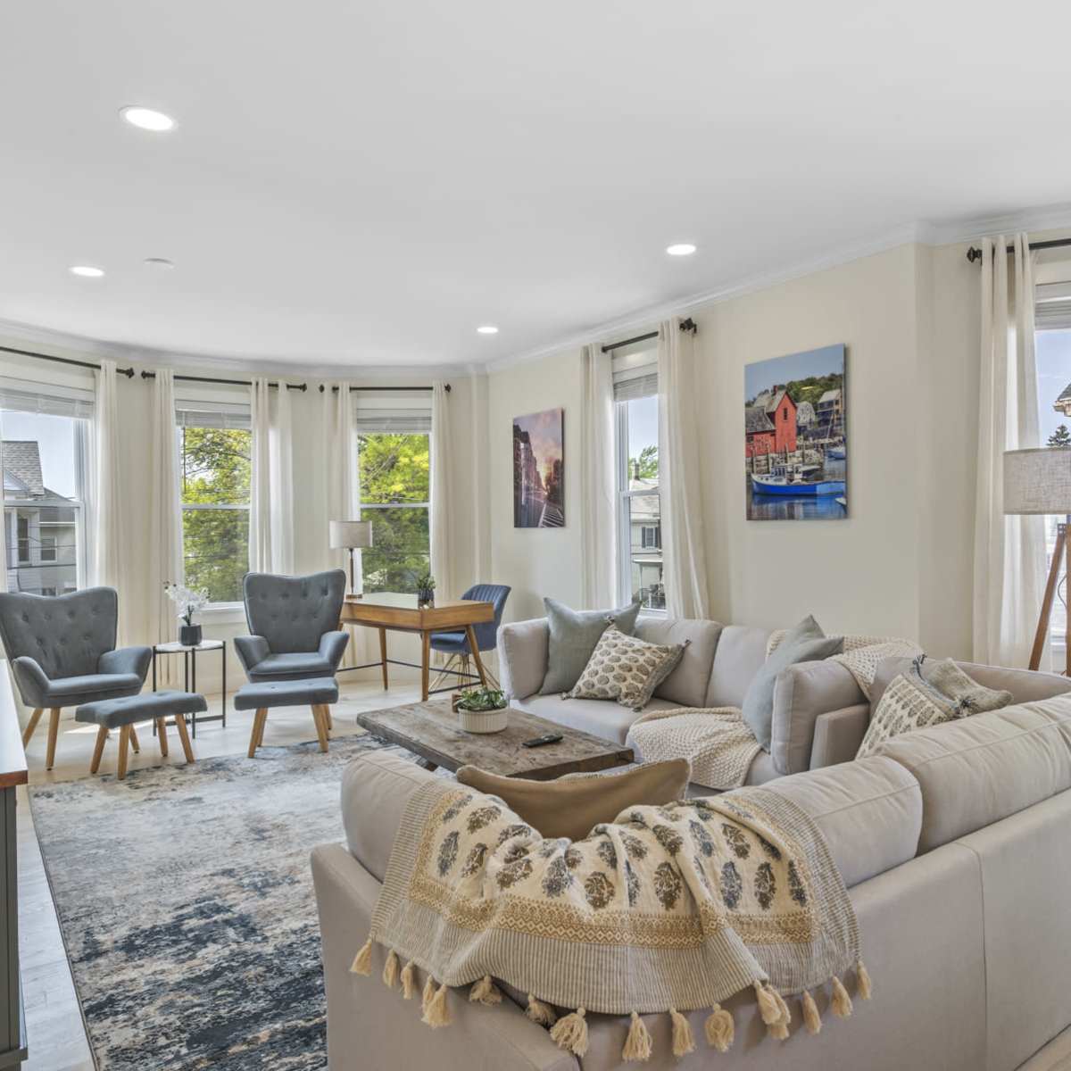 A modern living room features a large sectional sofa, two armchairs, and a coffee table, with large windows providing natural light.