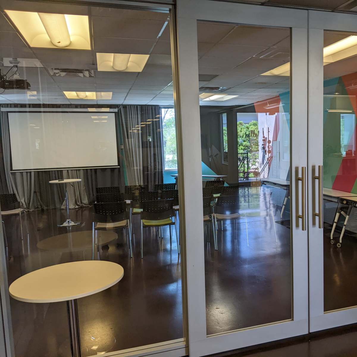 A glass-walled conference room with a modern design, featuring a table, chairs, and a colorful accent wall.