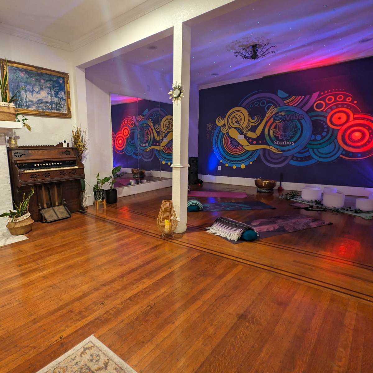 The room features a decorative fireplace and an adjacent area adorned with colorful murals, plants, and various seating arrangements on wooden flooring.