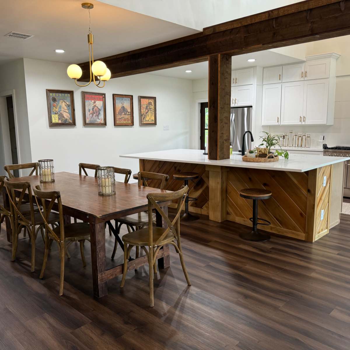 A spacious kitchen and dining area features a wooden table surrounded by chairs, with a large island and modern appliances in the background.