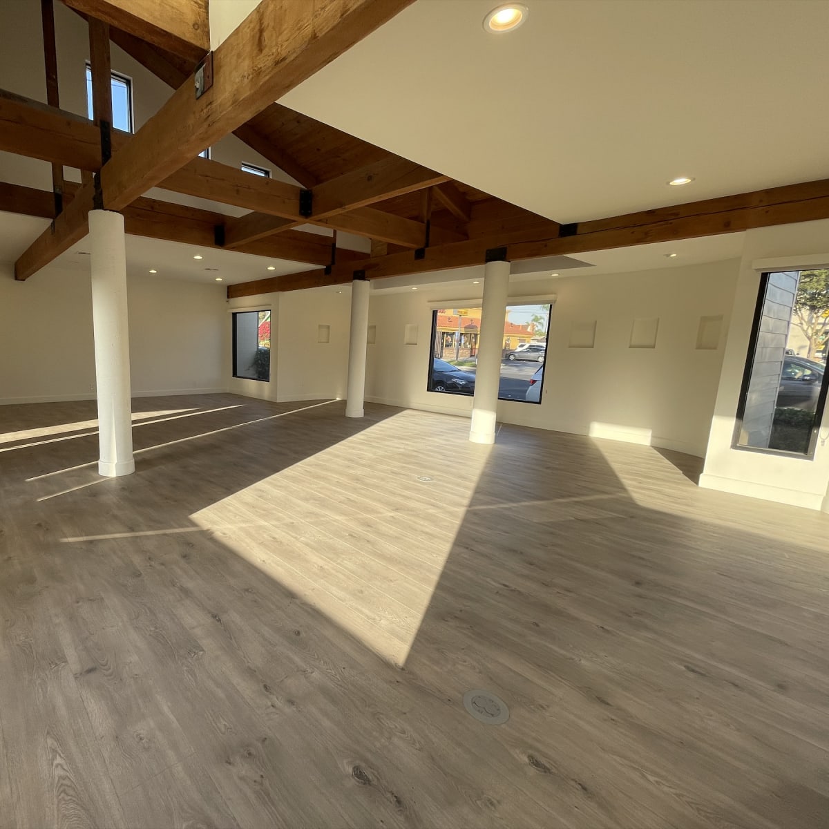 An empty room with wooden beams, large windows, and laminate flooring.