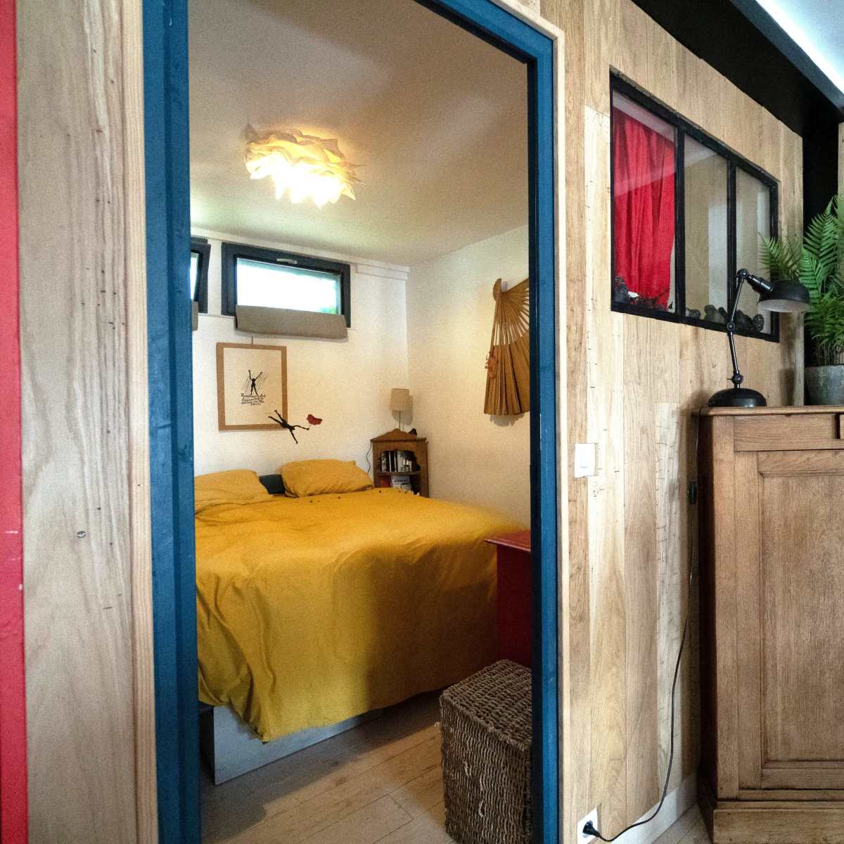 A compact room with a yellow bedspread, wooden furniture, and a small window, viewed through an open doorway.