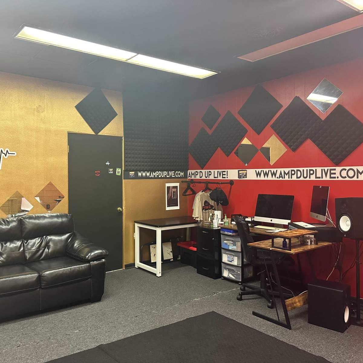 A music studio with black leather seating, soundproof walls, and a workstation equipped with computers and audio equipment.