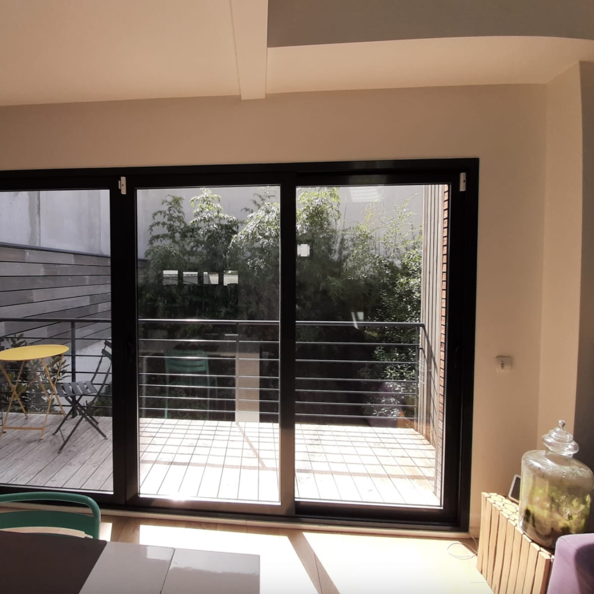 A modern indoor space with large glass doors opening to a wooden deck and greenery outside.