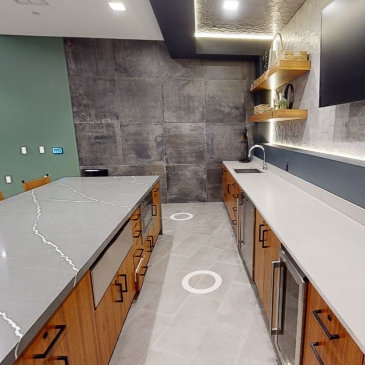 A modern kitchen area with gray and wooden cabinets, a spacious countertop, and a wall featuring hexagonal tiles.