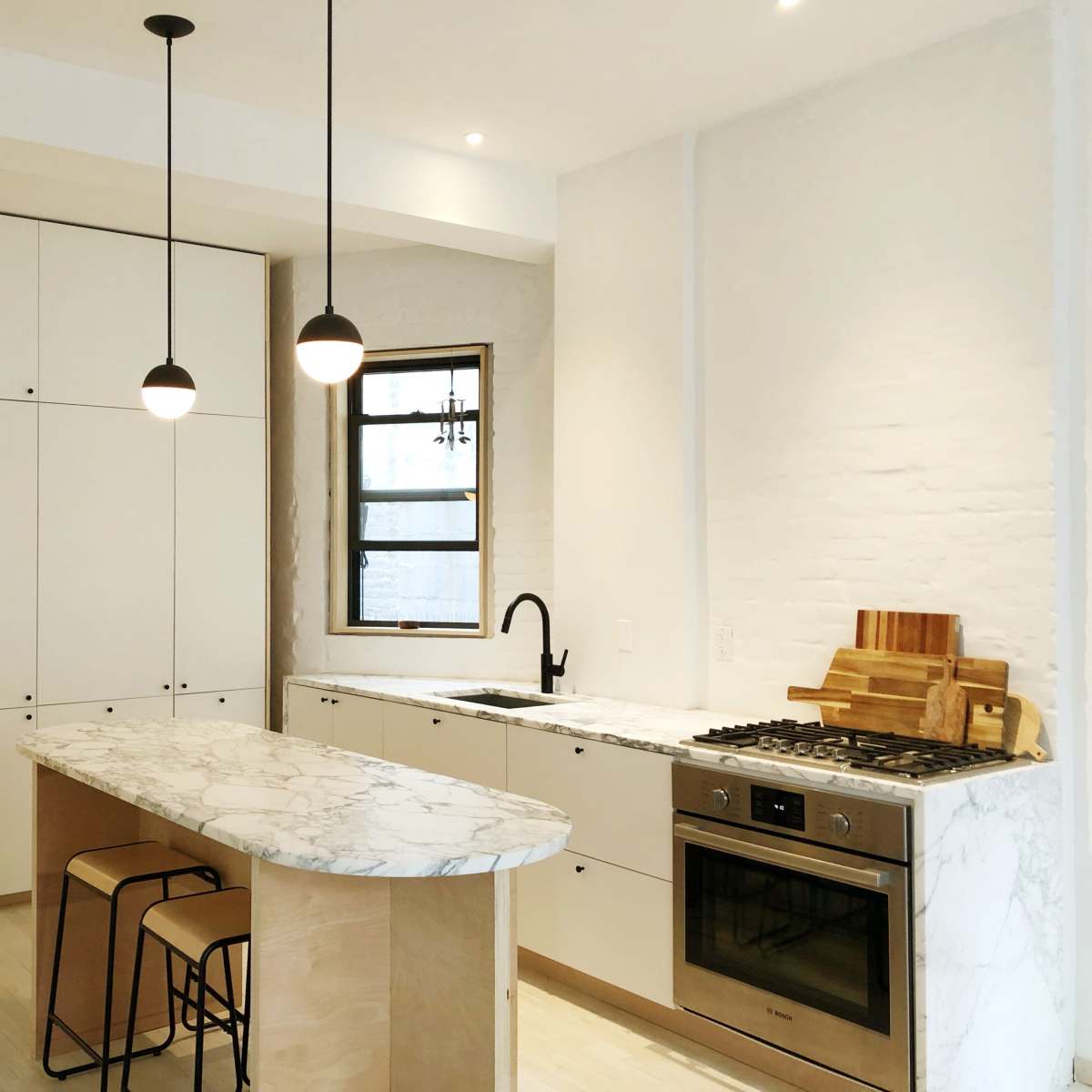 A modern kitchen features a marble-topped island, sleek cabinetry, stainless steel appliances, and pendant lighting.