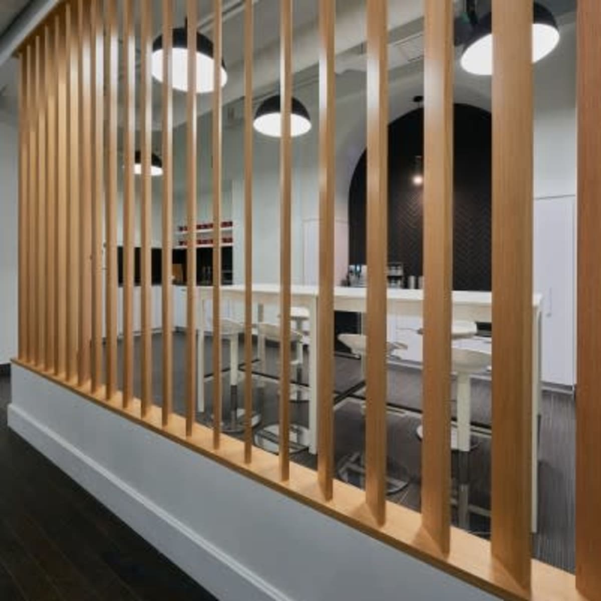A modern office space featuring a wood slatted partition with pendant lights hanging above a meeting area in the background.