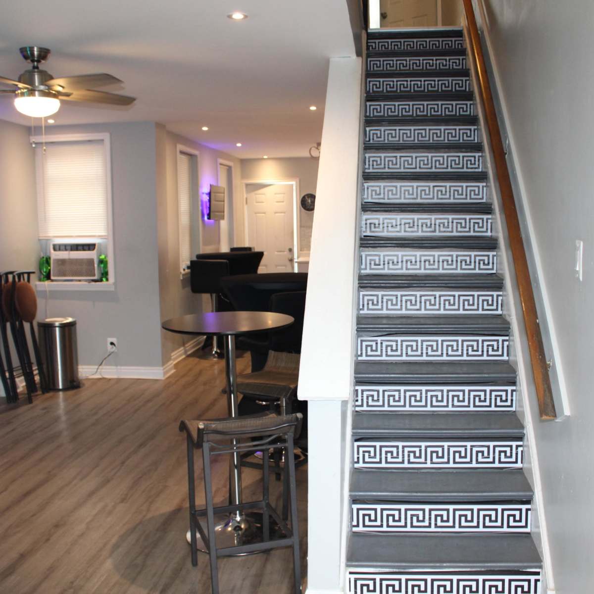 A modern interior with a staircase featuring patterned risers, leading to a living area with a seating arrangement and a wall-mounted television.
