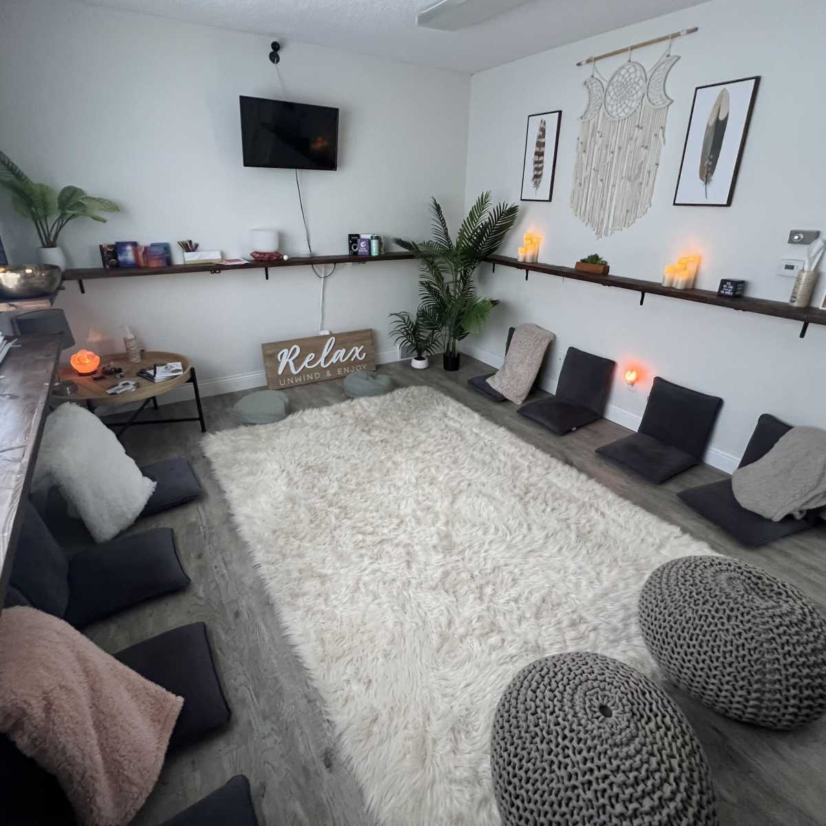 A tranquil relaxation room features a plush white rug, floor cushions, and decorative wall art, creating a serene environment.