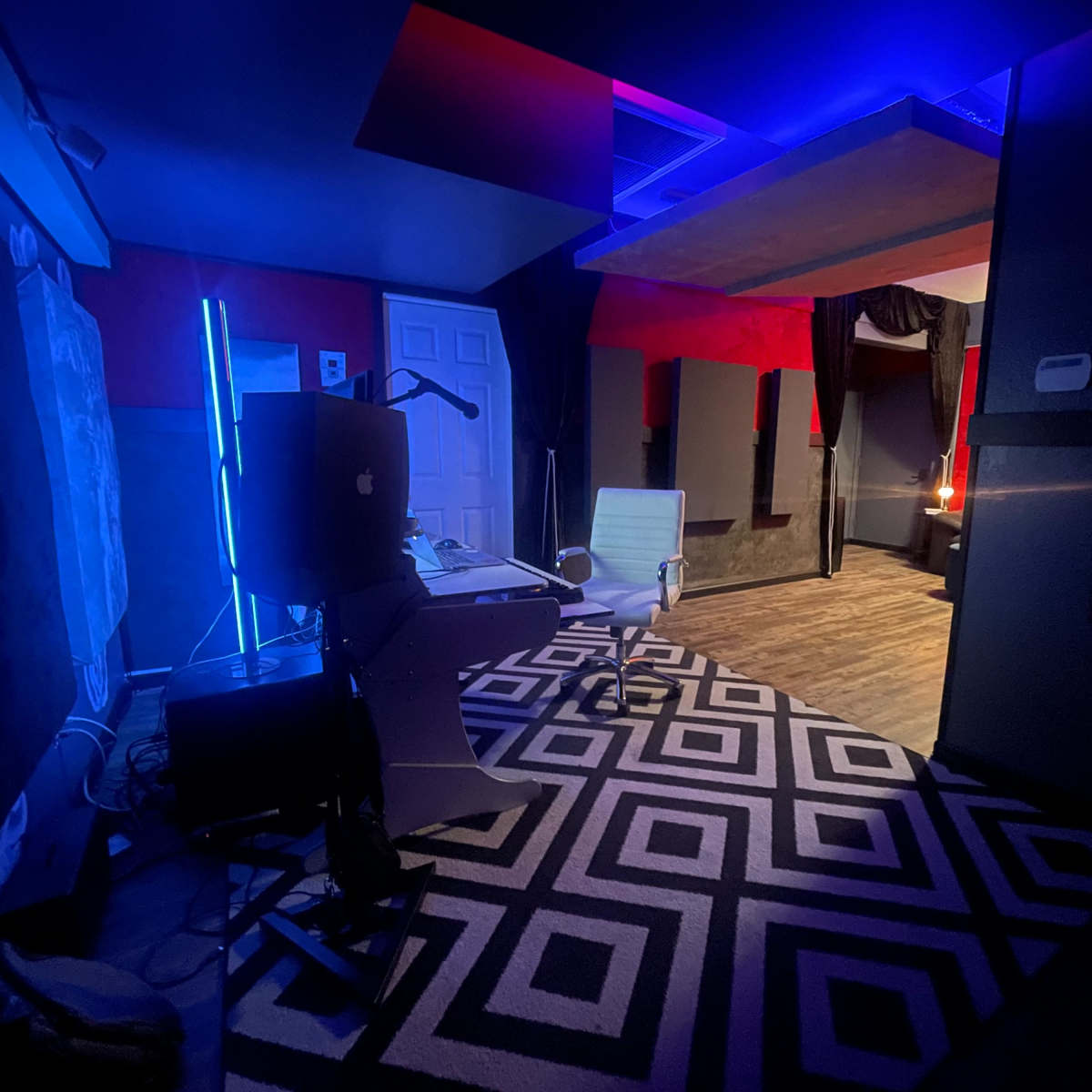 A dimly lit modern workspace featuring a desk with a computer, a chair, and a geometric patterned rug.