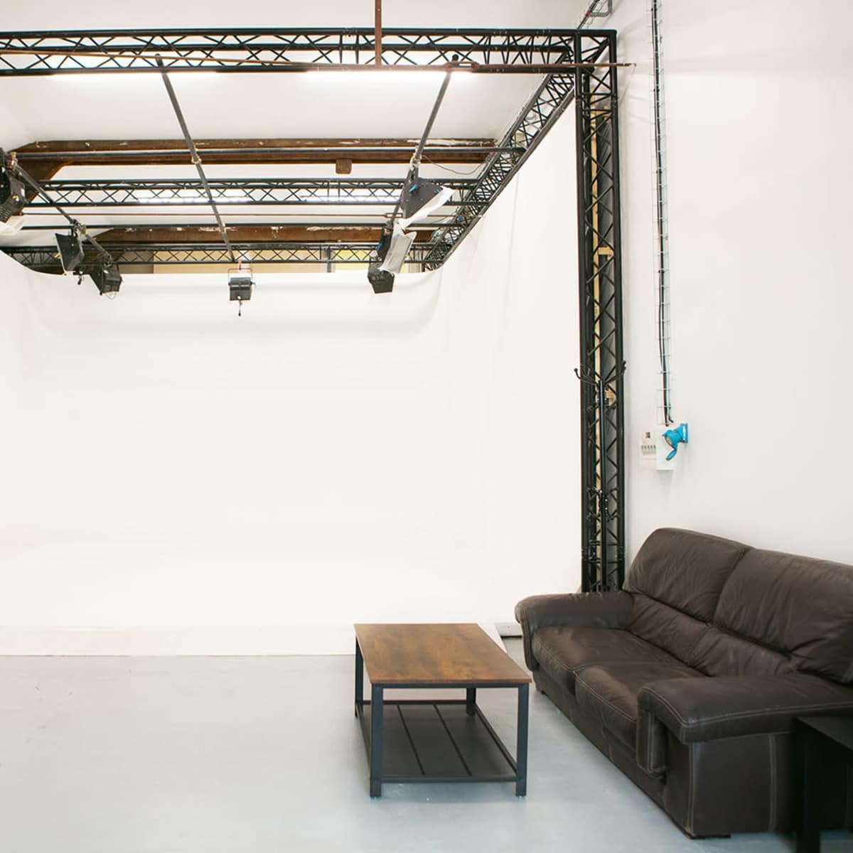 A photography studio with a large white backdrop, black support beams, and a brown leather couch next to a wooden coffee table.