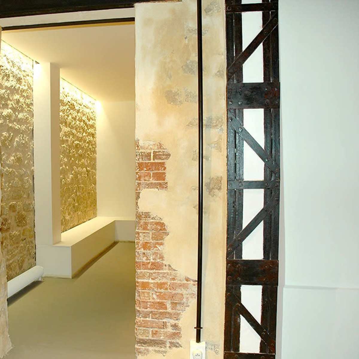 A minimalistic interior space with exposed stone walls and a corridor illuminated by linear lights.