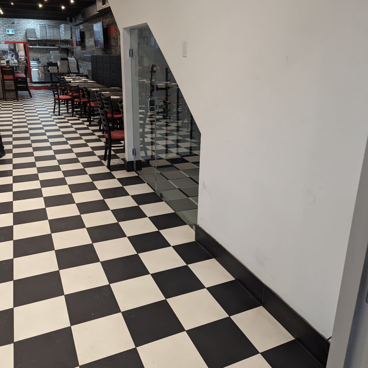A black and white checkered floor in a restaurant hallway leading to a glass wall and seating area.