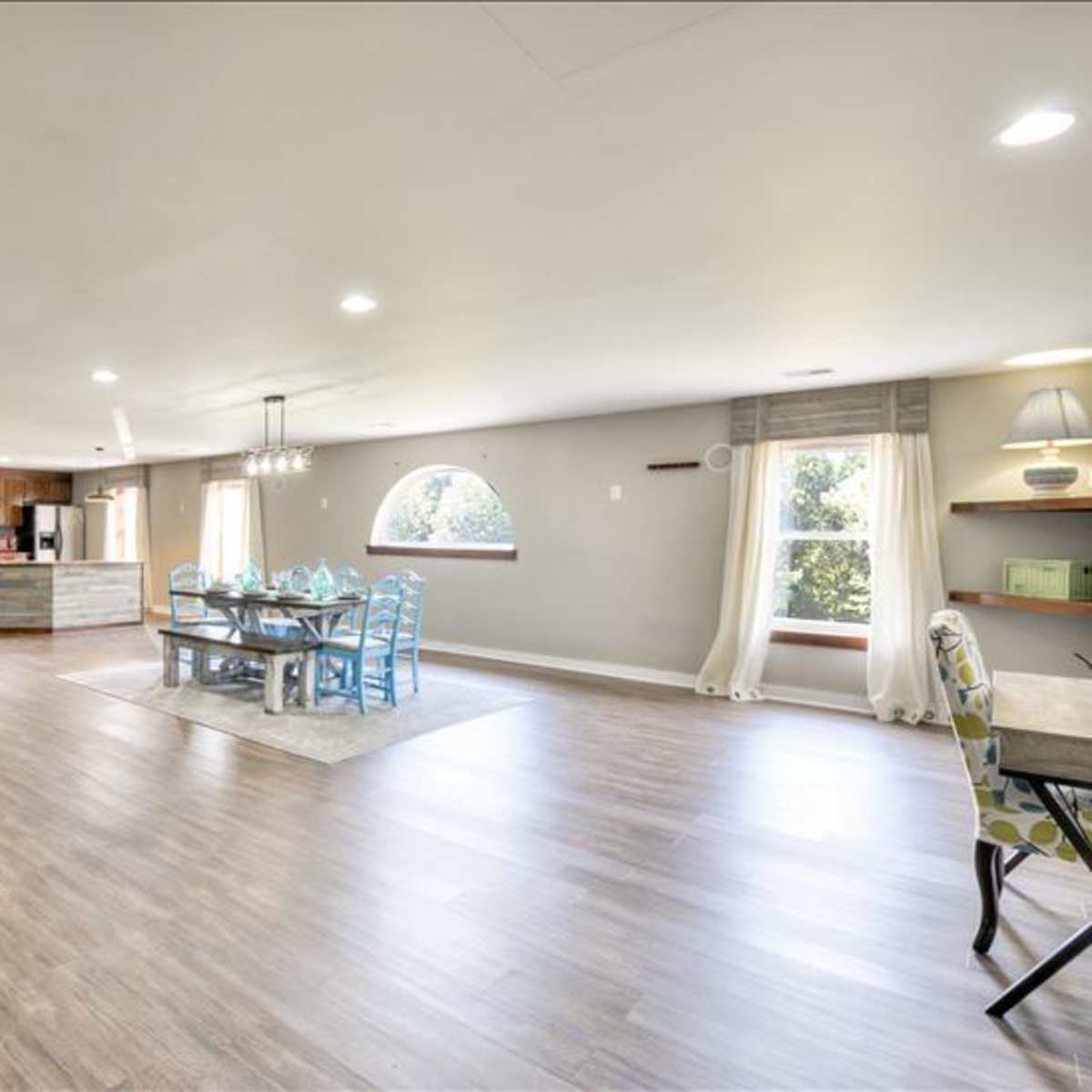 A spacious, open-concept living area features a dining table, a kitchen in the background, and large windows letting in natural light.