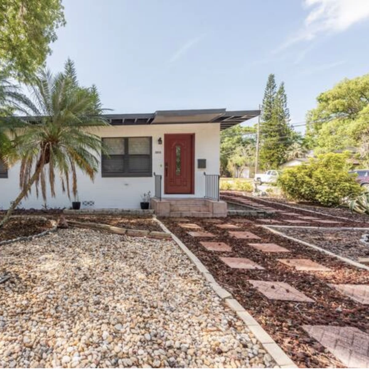 A single-story house with a red front door surrounded by landscaped gravel and greenery.