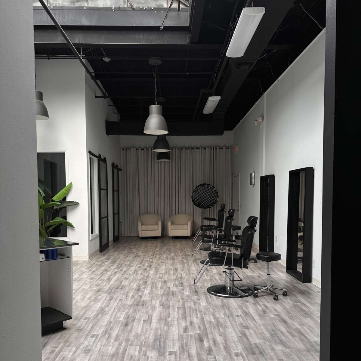 A spacious, modern interior with light wood flooring, two chairs at the far end, and several salon-style chairs along one side.