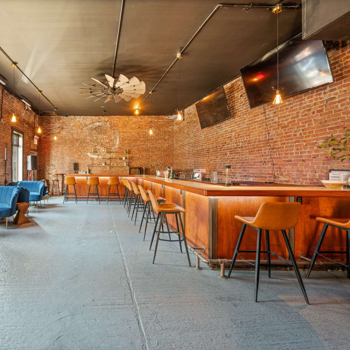 A spacious bar area with exposed brick walls, wooden furniture, and stools arranged around a central bar counter.