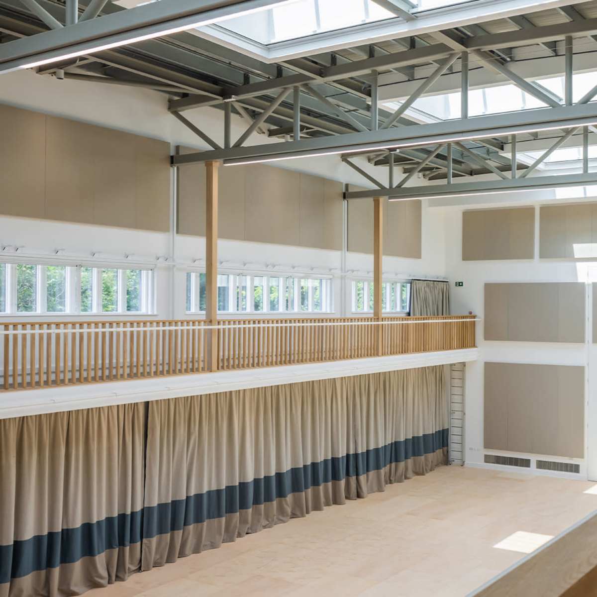 A spacious interior with large windows, high ceilings, and a balcony overlooking a wooden floor area.