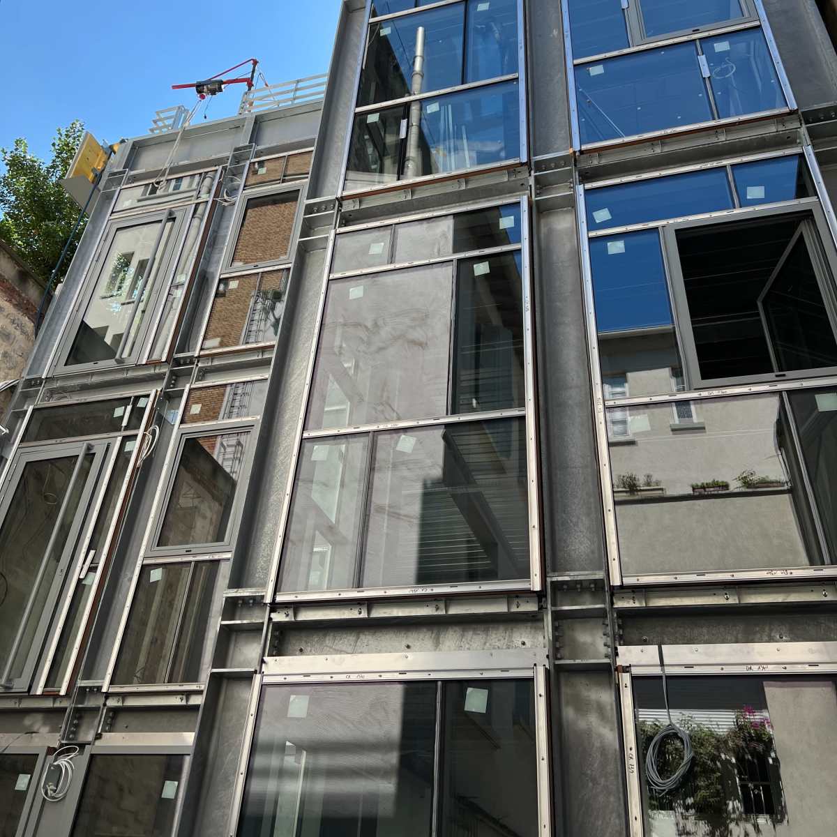 A modern building features a facade of large glass panels framed with metal, reflecting the blue sky above.