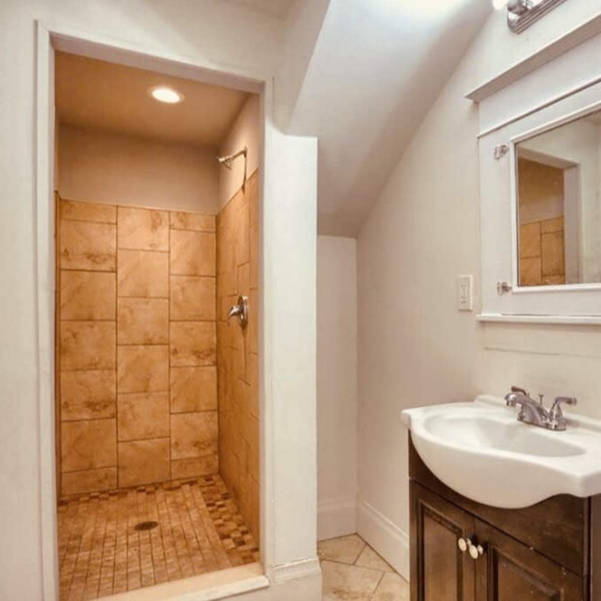 A small bathroom featuring a tiled shower area and a dark wood vanity with a sink and mirror.