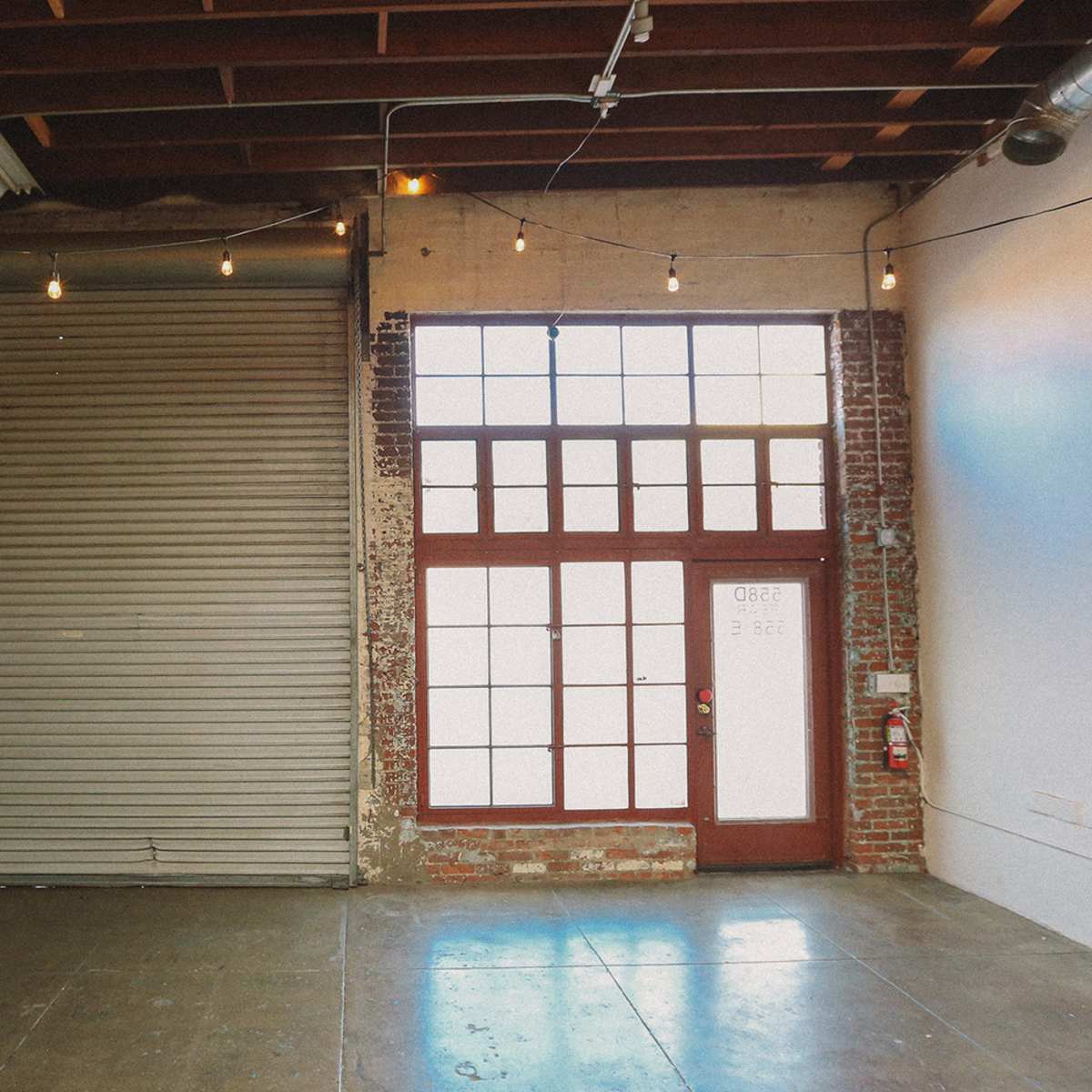 An industrial-style interior featuring a large roll-up door and a set of framed glass double doors with a brick wall background.