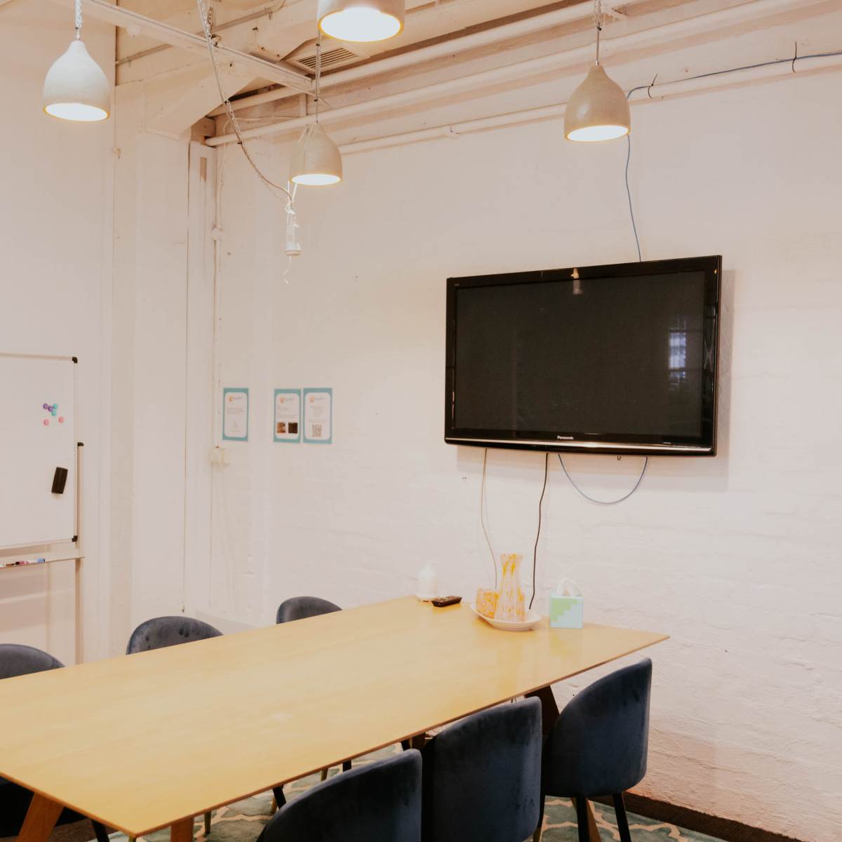 A meeting room features a long table surrounded by chairs, a whiteboard on wheels, and a mounted television on the wall.