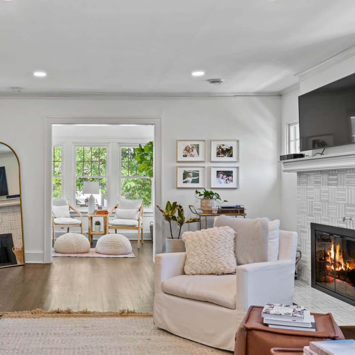 A cozy living room with a gray sofa, a white armchair, and a fireplace, leading to a bright dining area with a table and chairs partially visible.
